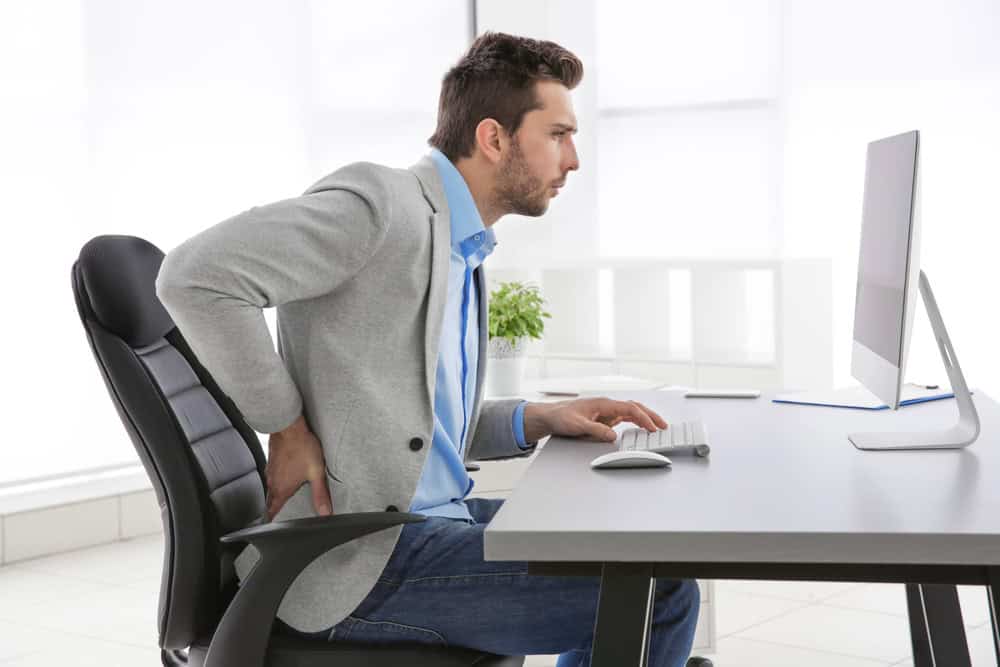 Man sitting at computer desk with bad posture rubbing his back