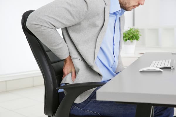 Man sitting at desk rubbing his painful lower back