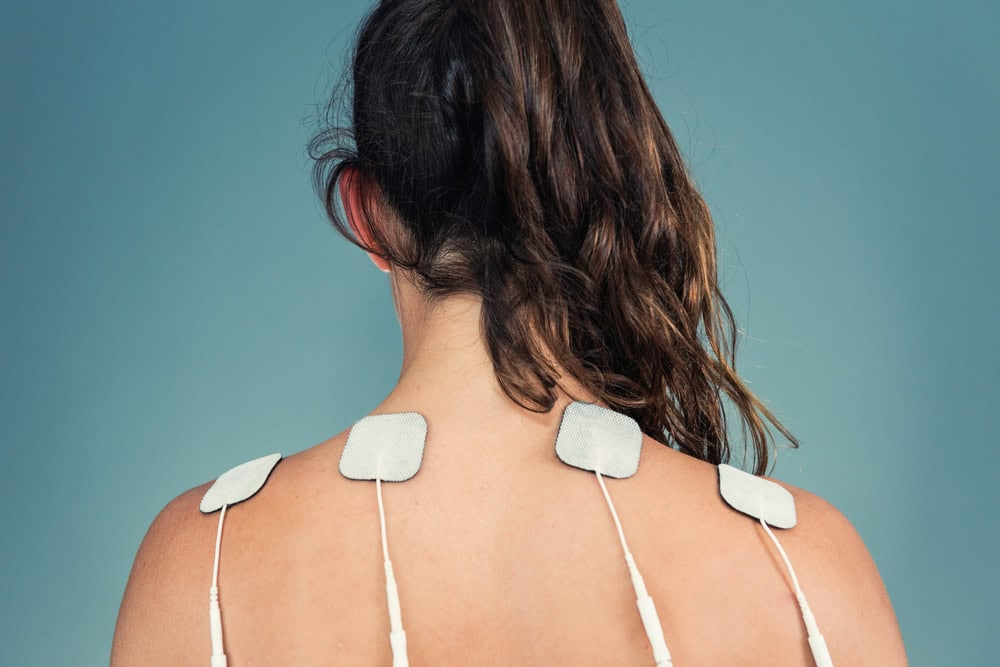 Woman with tens unit electrodes attached to shoulders and neck for home therapy.